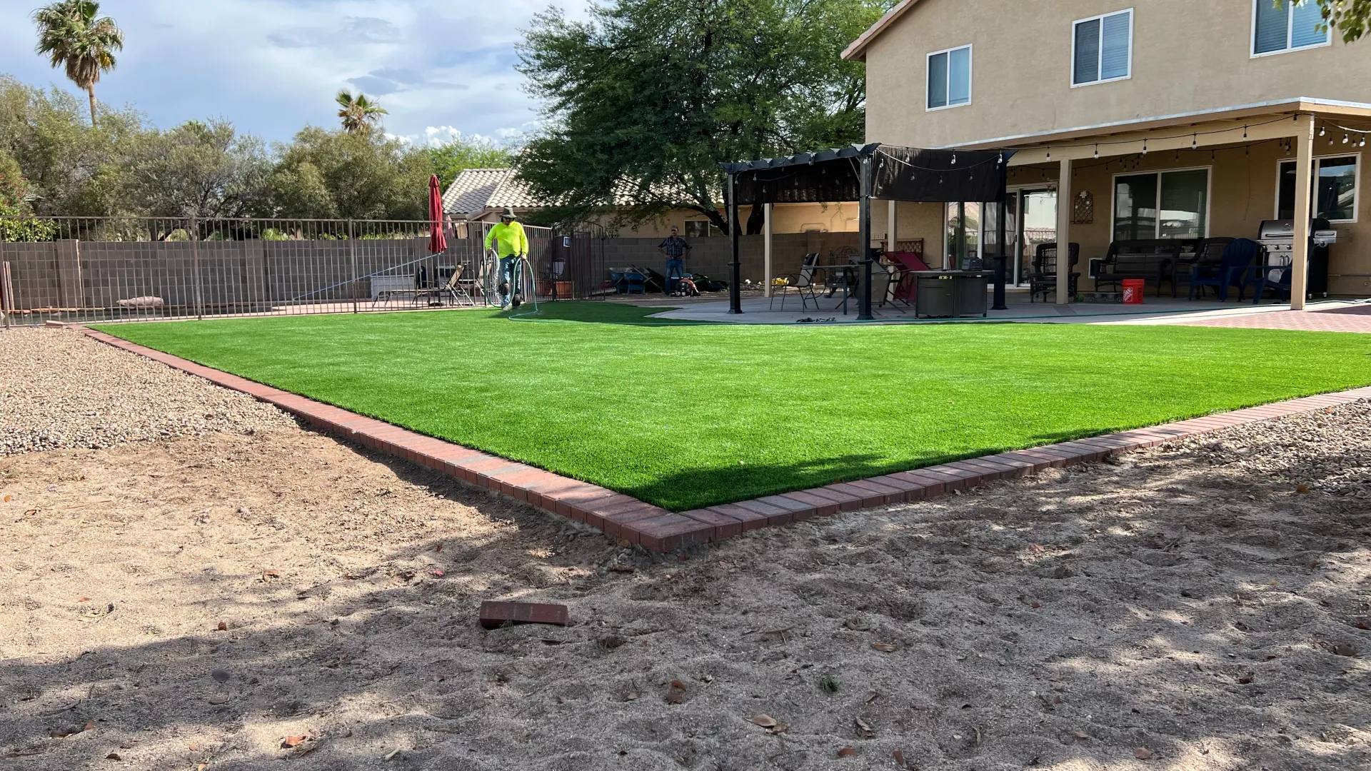 A rectangular, neatly edged lawn with bright green synthetic turf bordered by red brick pavers.