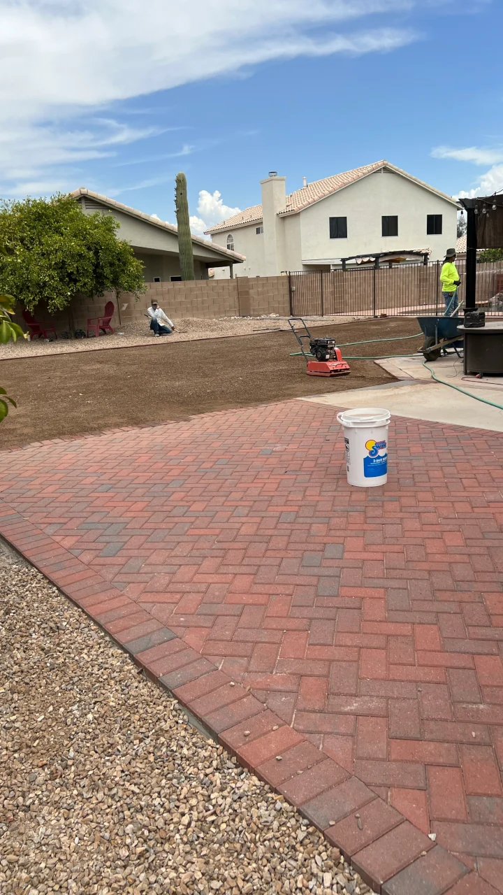 Backyard with red paver patio, gravel borders and workers preparing soil for landscaping.