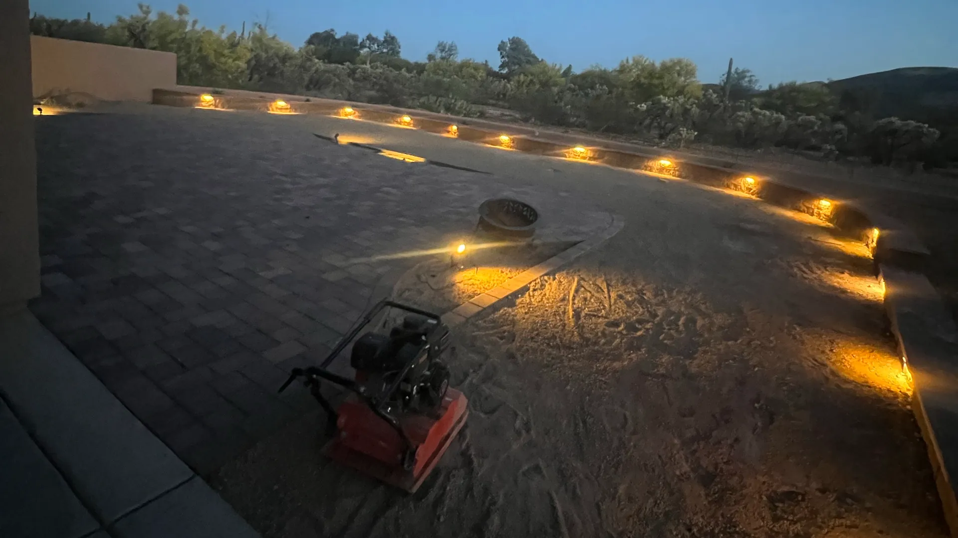 Low-angle dusk view of a large paved courtyard with warm, low-profile pathway lights installed along the perimeter.