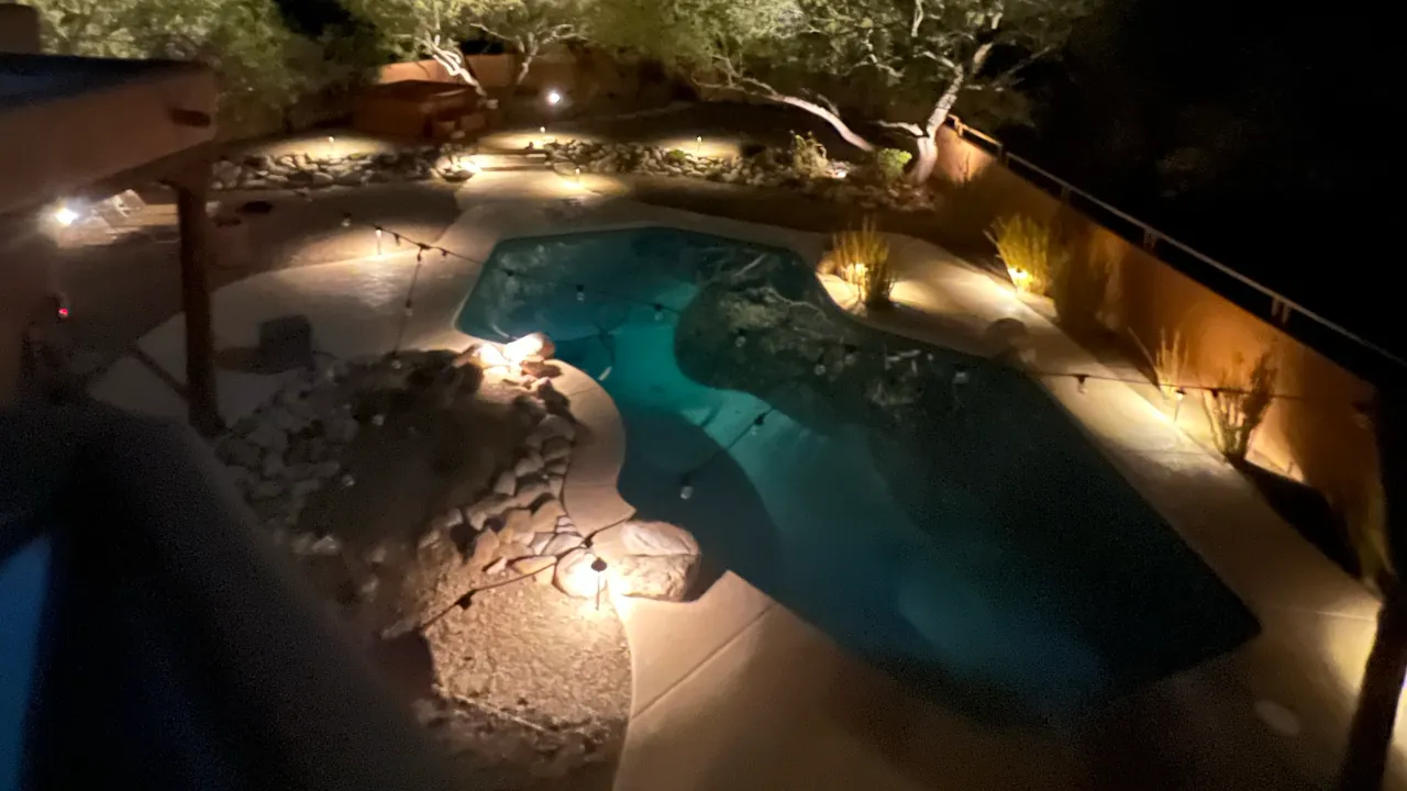 Warm accent lights placed around a pool edge and landscaping, casting amber light on the patio and water surface.