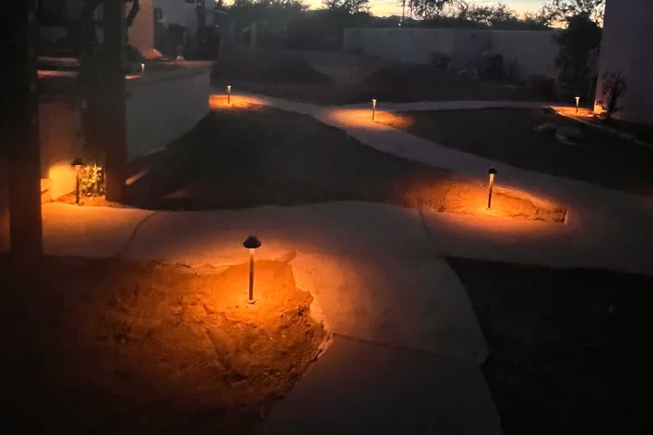 A winding concrete walkway flanked by short bollard-style lights, each emitting warm concentrated glow.