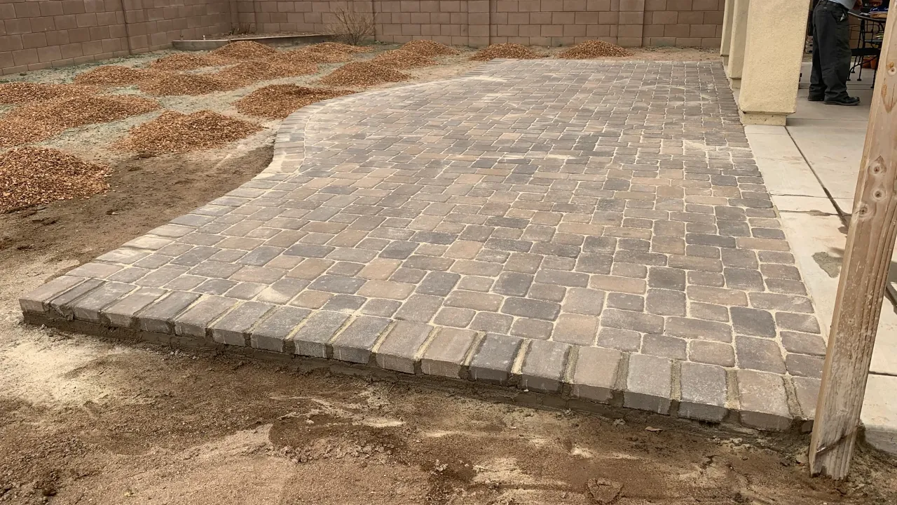 Newly installed interlocking paver patio with a raised edge, patterned pavers, and gravel beds.