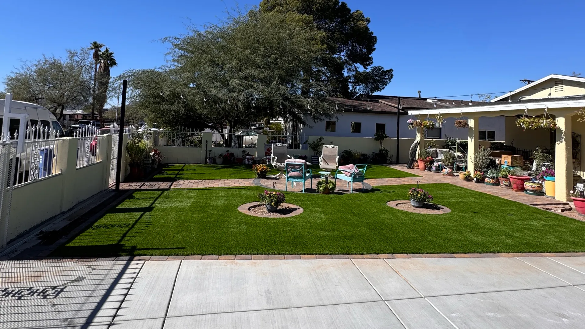 Backyard with travertine-accented patio seating area surrounded by artificial turf and garden furniture.