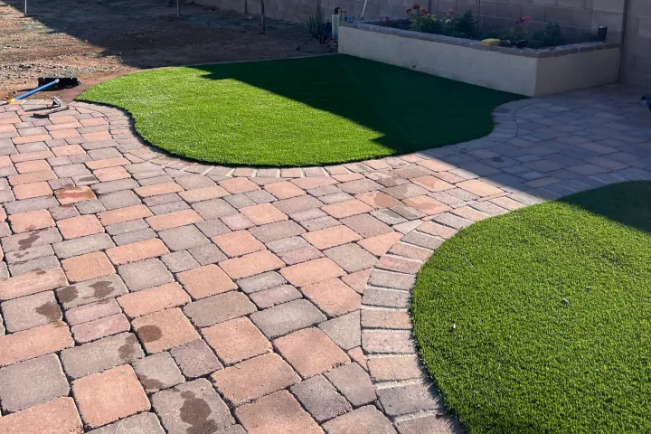 Curved artificial-turf inlays set within a patterned paver patio with raised garden bed.