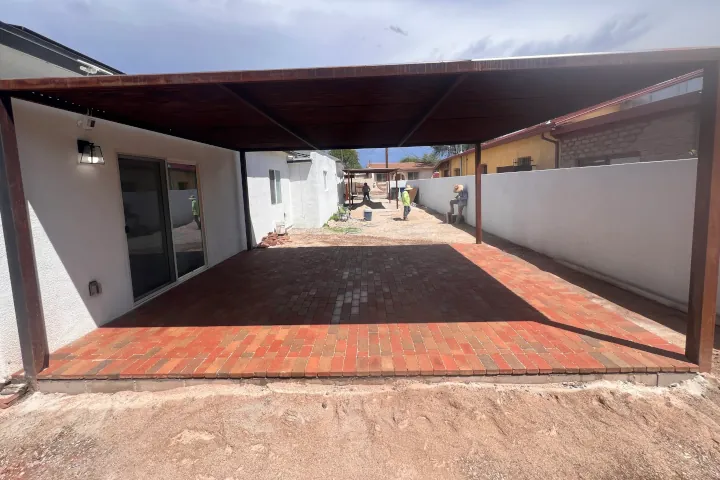 Covered outdoor patio with newly installed red travertine-style pavers under a wooden pergola.
