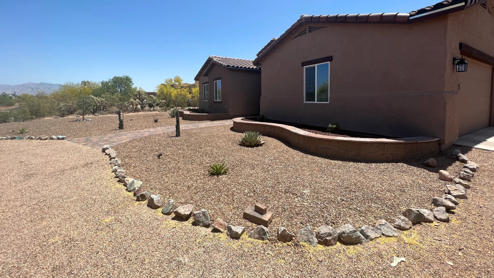 Desert-style front yard with gravel, rock border, and drought-tolerant plants beside a stucco home.